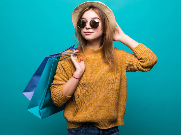 Young teen woman in sunglasses and hat holding shopping bags in her hands feeling so happiness isolated on green background